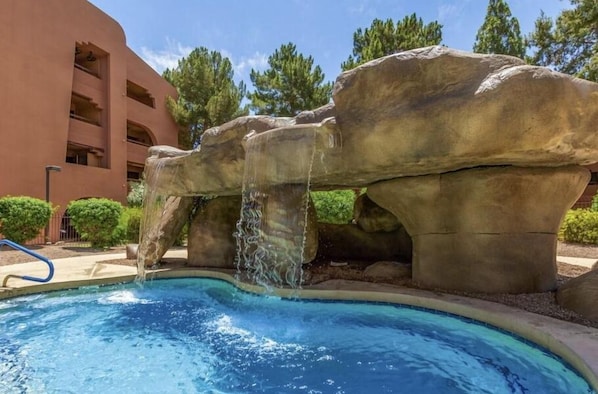 Ein Pool mit Felswasserfall, umgeben von einem Gebäude mit Balkonen.