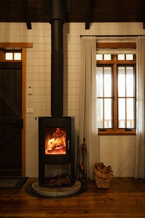 A wood-burning stove with a glass door, a window with curtains, and a wooden door. - The perfect spot for family and friends (Bright)