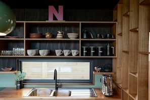 A kitchen with wooden shelves, a large window, and a sink. - The perfect spot for family and friends (Bright)
