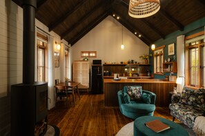 A cozy interior with a wooden ceiling, a central island with kitchen appliances, a seating area with a sofa and chairs, and a fireplace. - The perfect spot for family and friends (Bright)