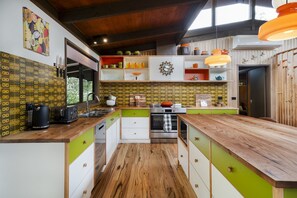 A kitchen with a wooden countertop, a sink, and a stove. There are cabinets with green and white doors, and a wall clock. - The perfect spot for family and friends (Bright)