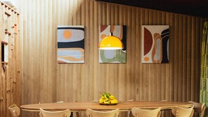 Un tavolo da pranzo in legno con sei sedie, una ciotola di frutta sul tavolo e tre dipinti astratti appesi al muro.