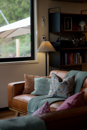 A cozy living room with a leather sofa, a lamp, and a bookshelf. - The perfect spot for family and friends (Bright)