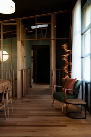 A wooden interior with a dining area, a green chair, and a staircase leading to a dark room. - The perfect spot for family and friends (Bright)