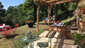 Een terras buiten met rieten dak, stenen vloer, metalen meubilair en potplanten.