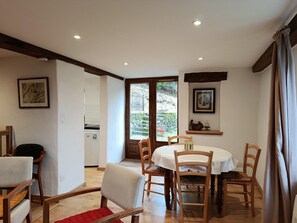 A dining area with a round table and chairs, a kitchen visible through an open door, and framed artwork on the walls. - Le Verger - VEBRON - Gîte (VEBRON)