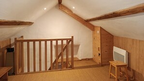 Een kamer met een schuine balken plafond, een trap, een houten poort, een kleine tafel en een televisie.