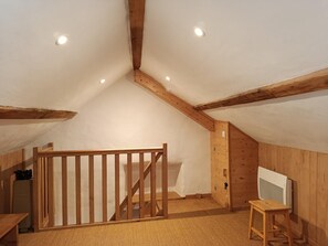 A room with a sloped ceiling, wooden beams, a staircase, a wooden gate, a small table, and a television. - Le Verger - VEBRON - Gîte (VEBRON)