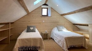 Een gezellige zolderkamer met twee bedden, houten balken, een klein raam en een nachtkastje.