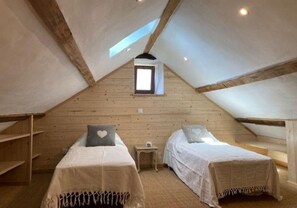 A cozy attic bedroom with two beds, wooden beams, a small window, and a nightstand. - Le Verger - VEBRON - Gîte (VEBRON)