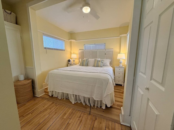 A bedroom with a bed, bedside tables, lamps, a ceiling fan, and a window with blinds.