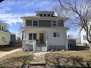 A two-story house with a front porch, a front door, and a small front yard.