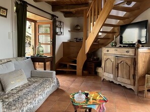A living room with a sofa, a wooden staircase, a television, and a table with a tray. - Le Gîte des Oiseaux - VEBRON (VEBRON)