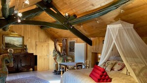 Ein Schlafzimmer mit Himmelbett, Holzbalkendecke, einer Pferdeskulptur und einem Essbereich mit Tisch und Stühlen.