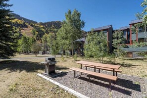 A picnic area with a grill and benches, surrounded by trees and buildings. - Telluride Trails Retreat: 3BR/2BA - Hot Tub/Sauna (Telluride)