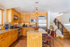 A kitchen with wooden cabinets, a central island, a stainless steel refrigerator, and a staircase. - Telluride Trails Retreat: 3BR/2BA - Hot Tub/Sauna (Telluride)