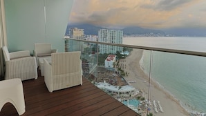 Een balkon met rieten meubilair met uitzicht op een strand en stadsbeeld.