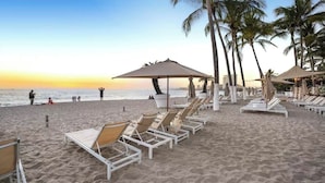 Een strand met ligbedden, parasols en palmbomen.