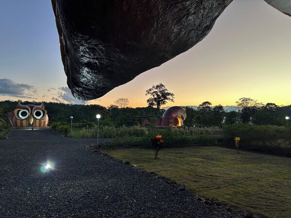 Un sendero conduce a una gran formación rocosa con una escultura de un búho y un edificio de forma abovedada.