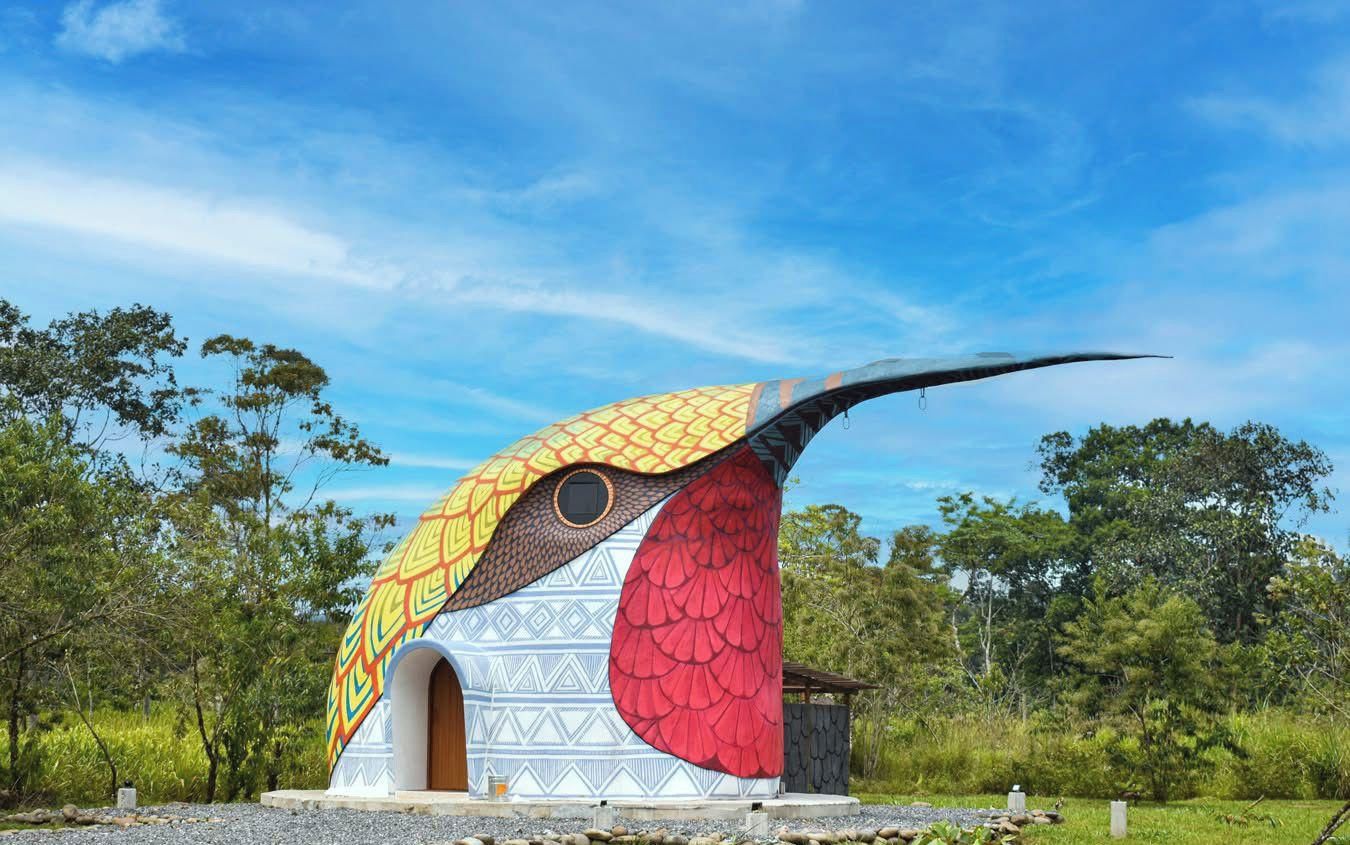 A bird-shaped structure with a patterned exterior, set in a natural landscape with trees and clear skies.