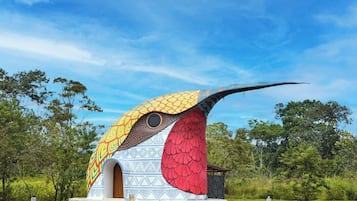 A bird-shaped structure with a patterned exterior, set in a natural landscape with trees and clear skies.