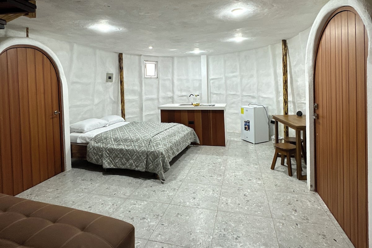 A compact bedroom with a bed, a small desk, a chair, and a sofa.