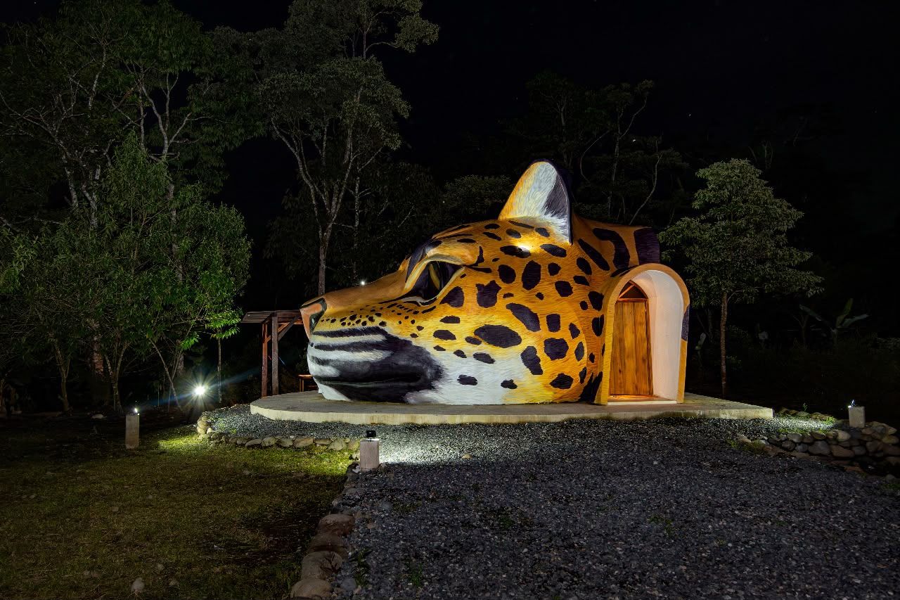 Una gran escultura iluminada de la cabeza de un jaguar con una puerta de madera.