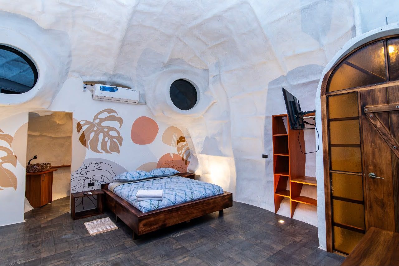 A bedroom with a bed, a wooden wardrobe, a TV, and a circular window.