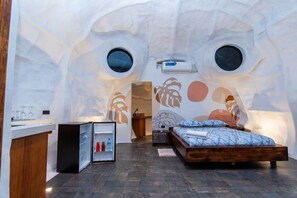 A modern room with a unique arched ceiling, a bed, a small kitchenette, and a large window. - Animal Glamping (Pomona)