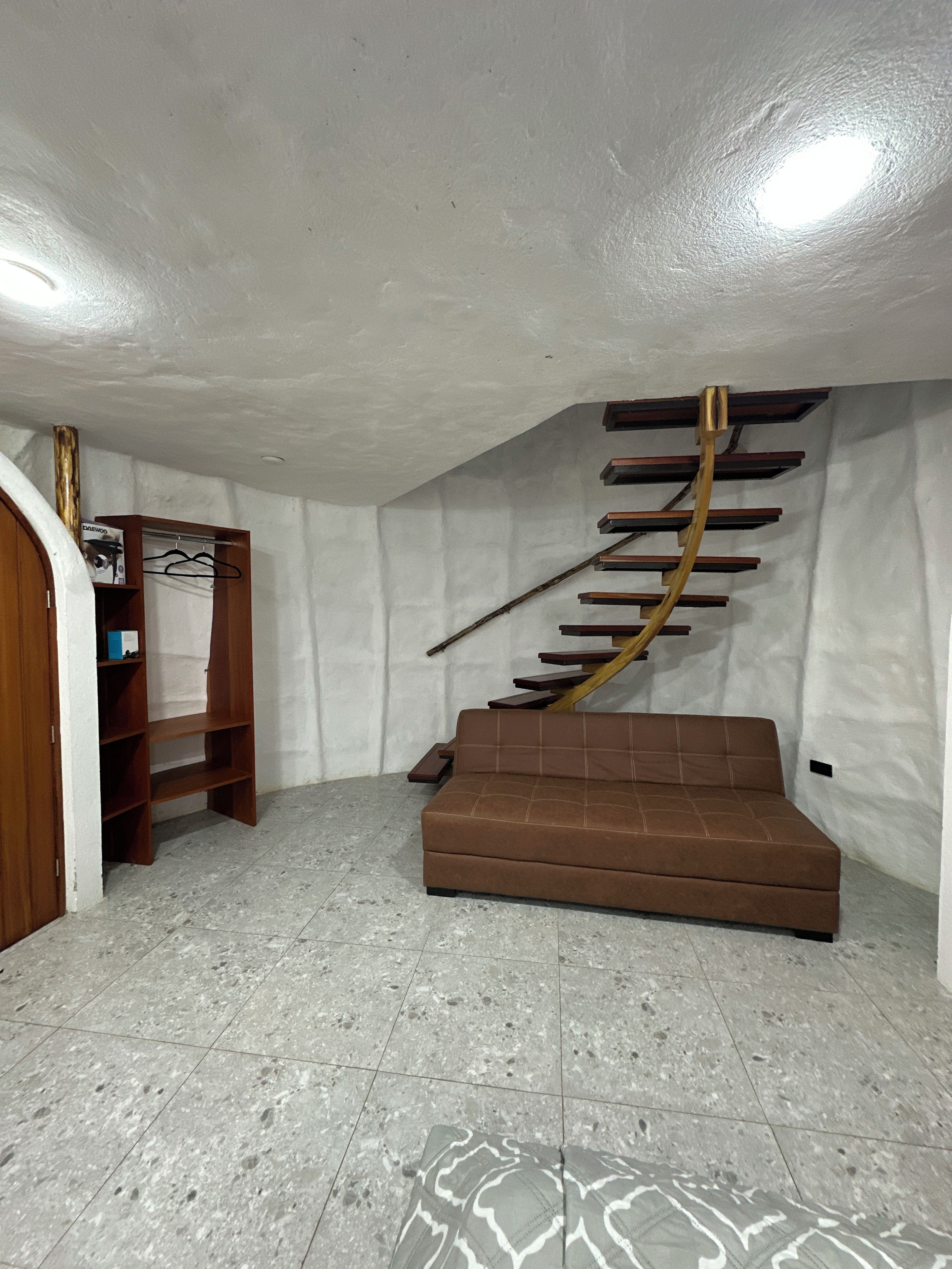 A room with a brown sofa, a wooden ladder-like structure, and a tiled floor.