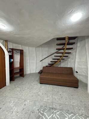 A room with a brown sofa, a wooden ladder-like structure, and a tiled floor. - Animal Glamping (Pomona)