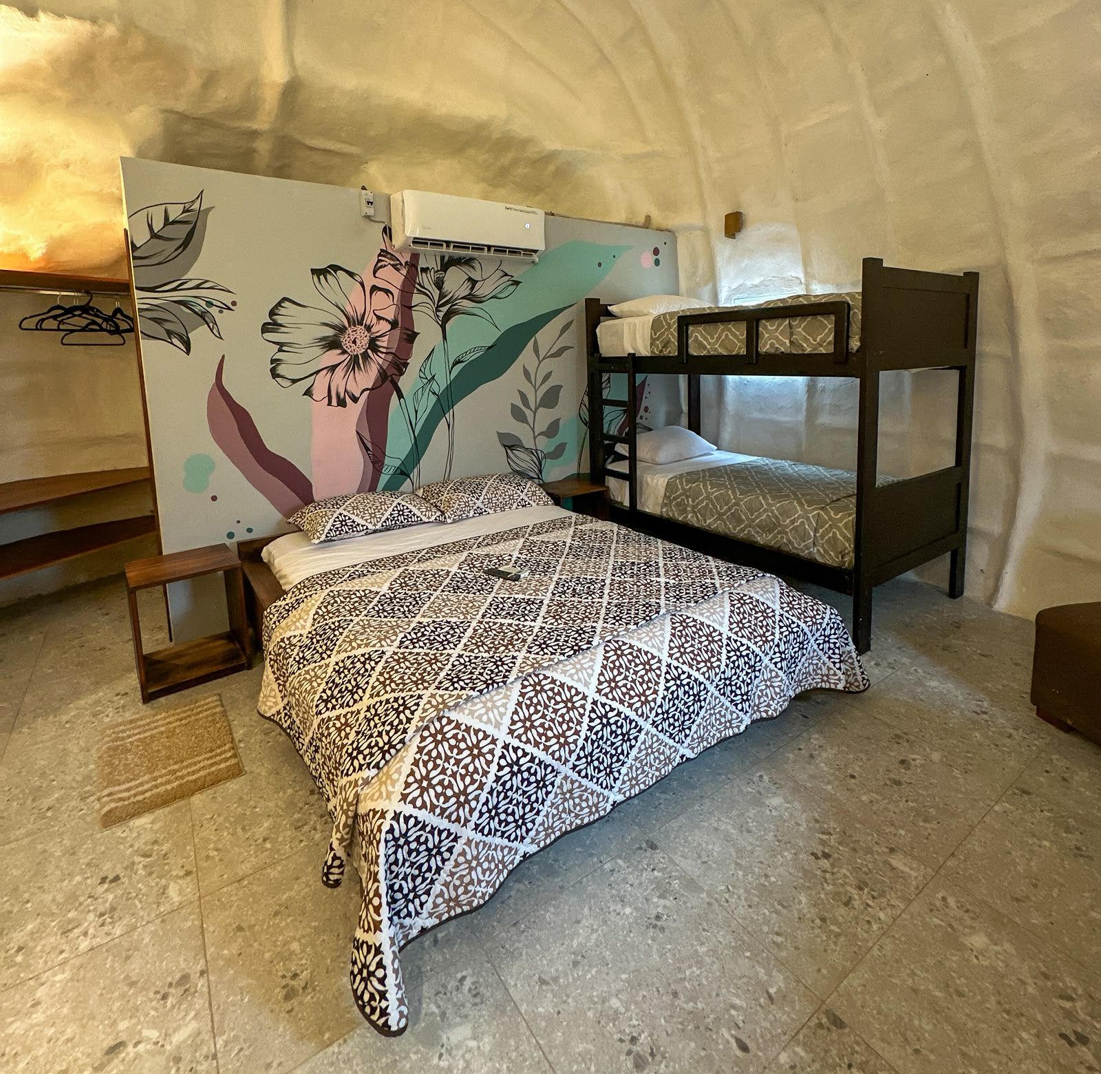 A bunk bed with a patterned bedspread, a wall with a floral mural, and a small wooden table.