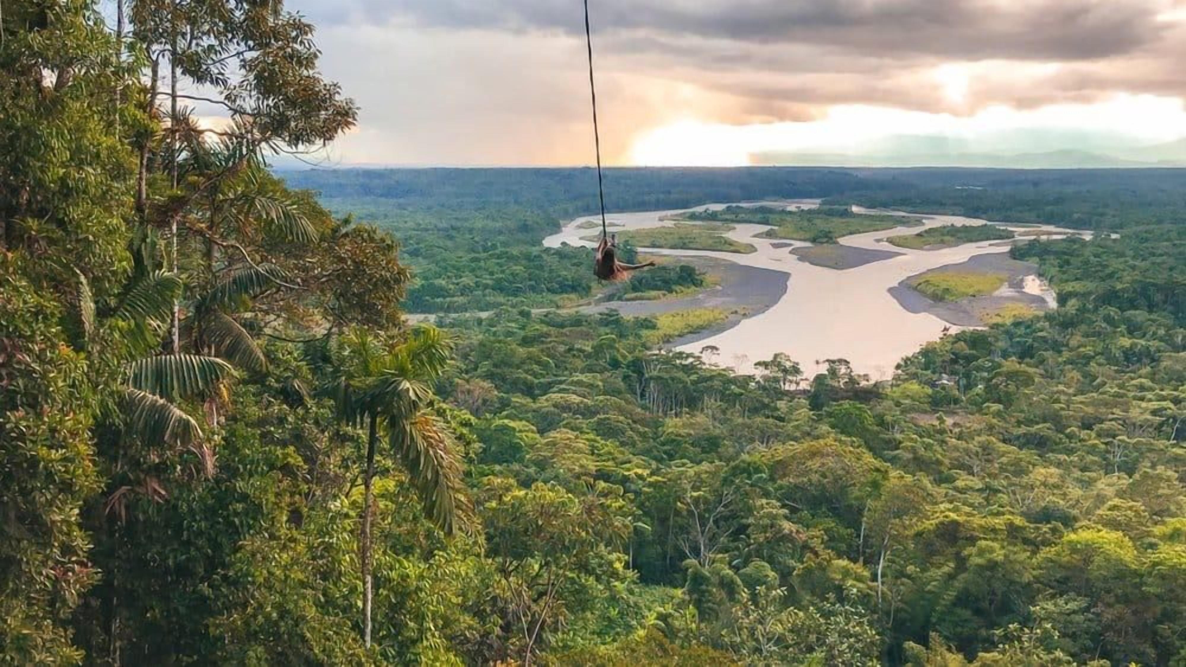 Een junglelandschap met een rivier en een persoon op een zipline.