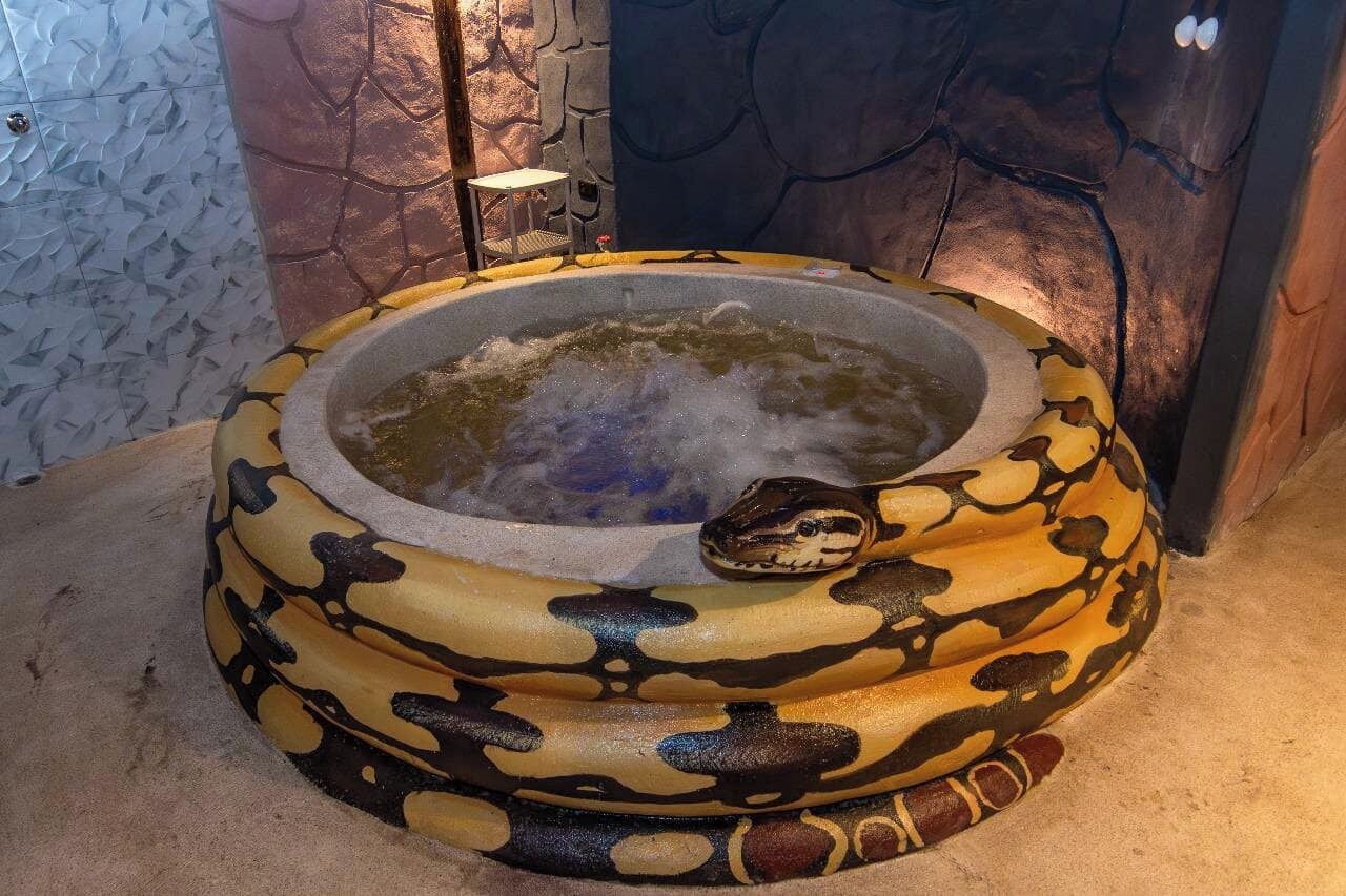 A hot tub with a snake design, surrounded by stone walls and a small table.