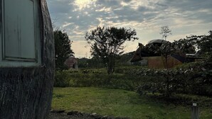 A building with a curved exterior wall, a paved pathway, and a grassy area with trees and shrubs. - Animal Glamping (Pomona)