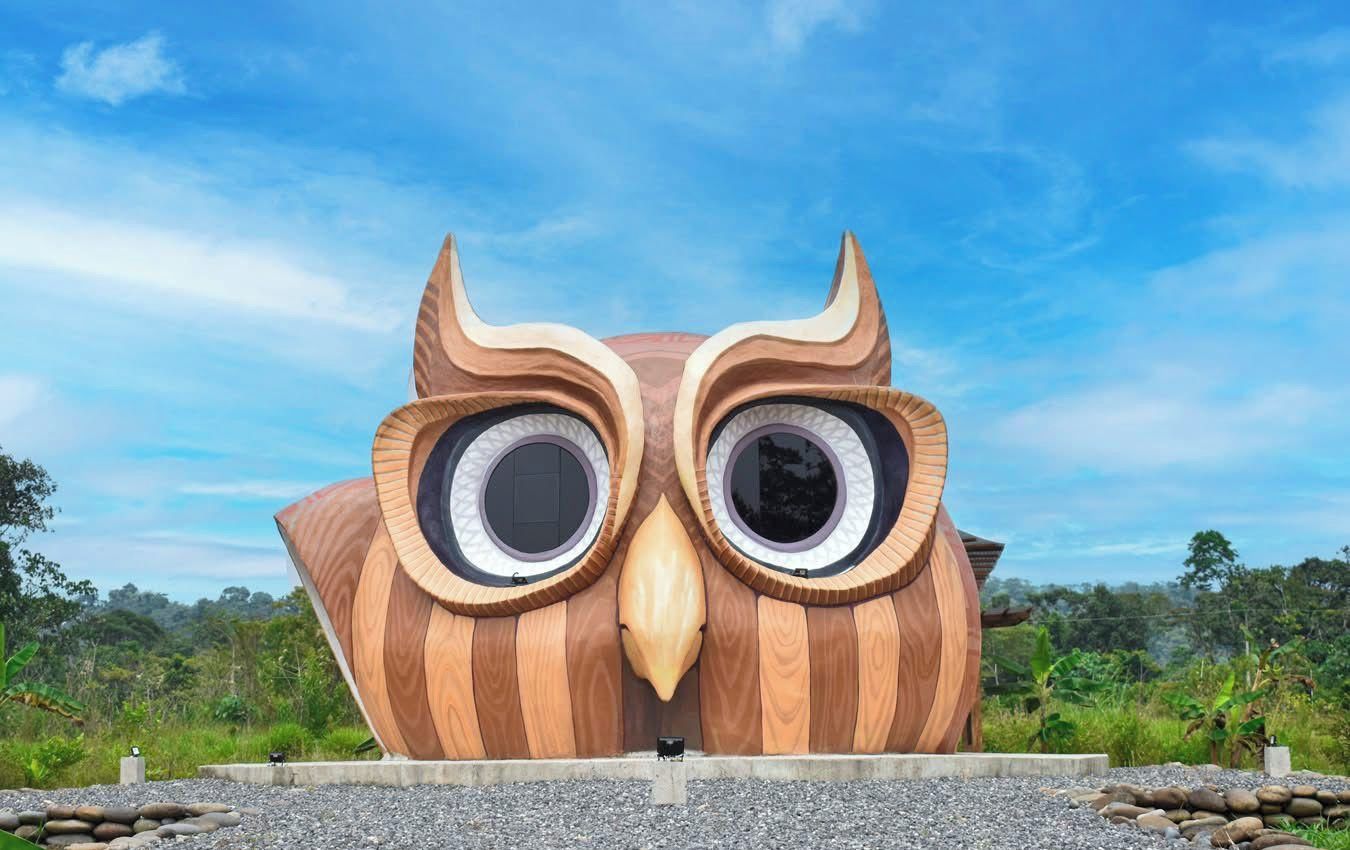 A large wooden sculpture of an owl with circular eyes and a beak, set against a clear sky.