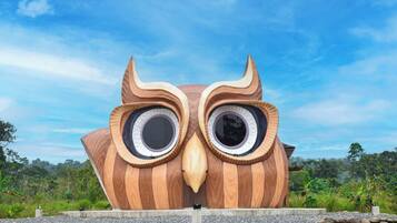 A large wooden sculpture of an owl with circular eyes and a beak, set against a clear sky.