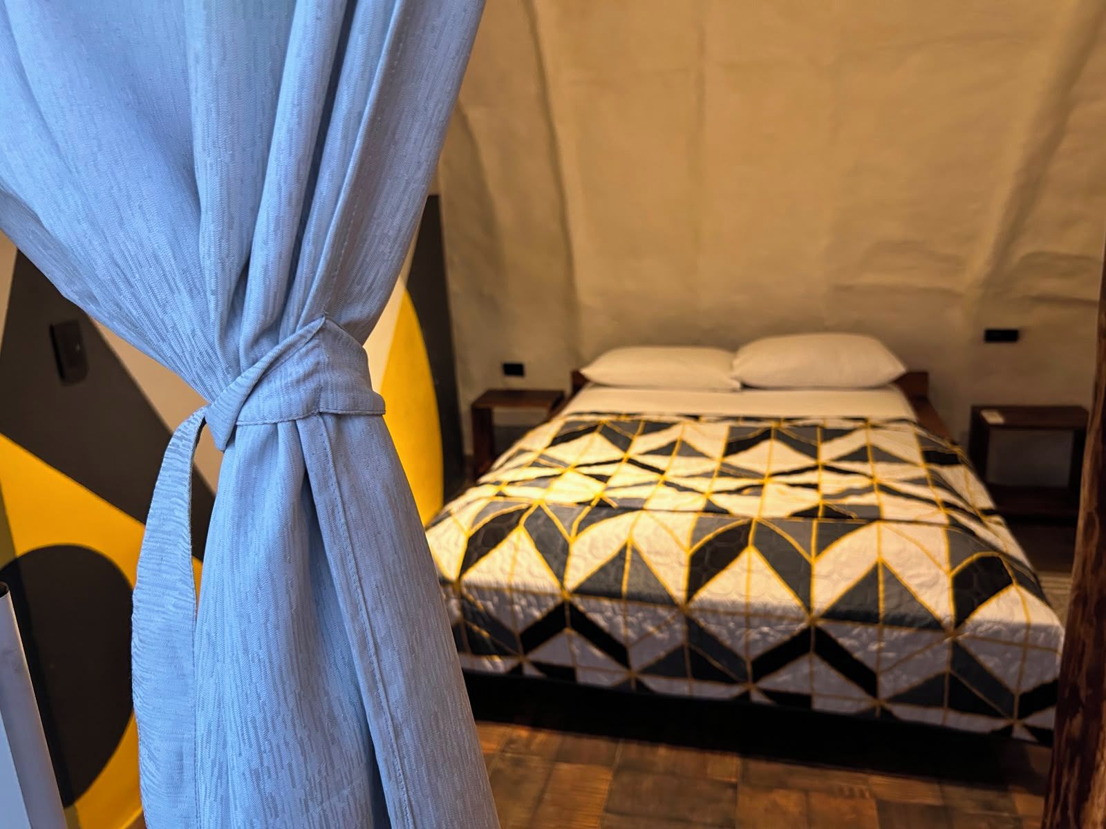 A room with a bed, a nightstand, and a curtain.