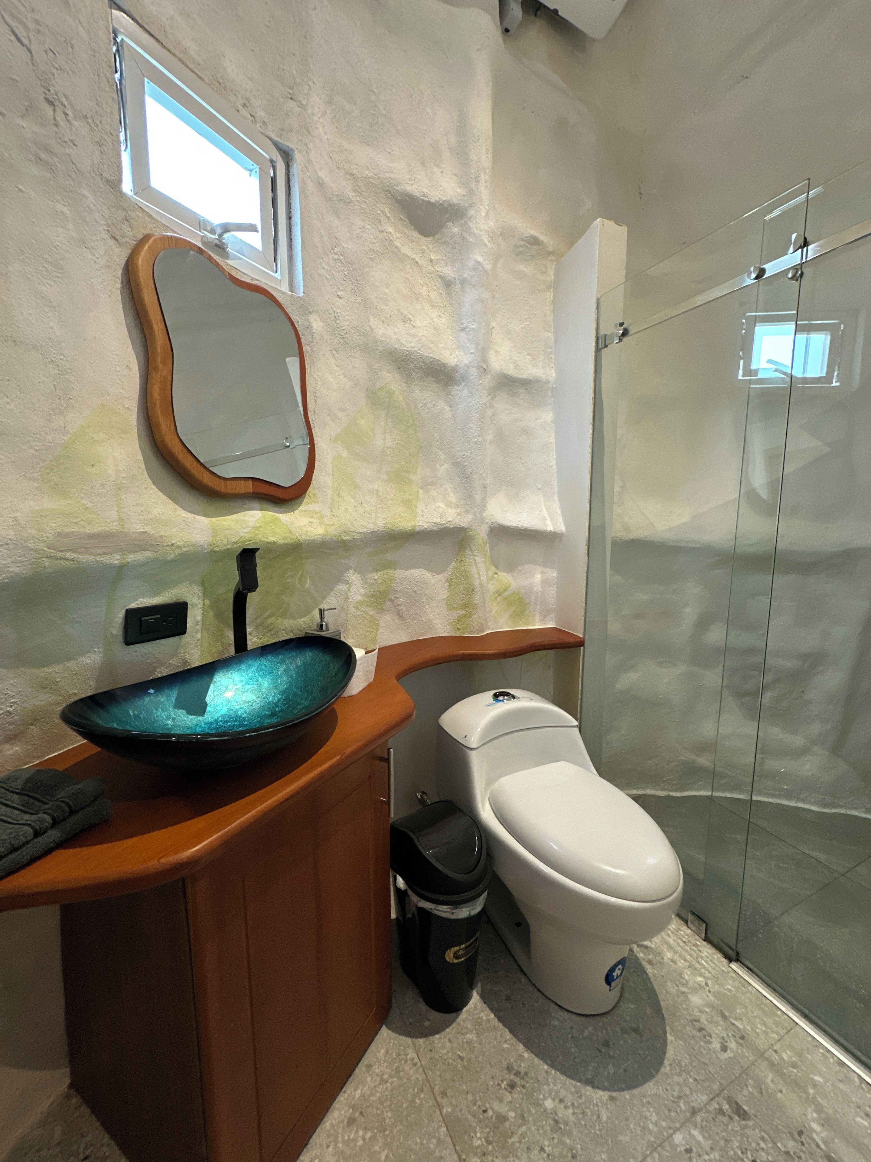 A bathroom with a wooden vanity, a glass sink, a toilet, and a shower enclosure.