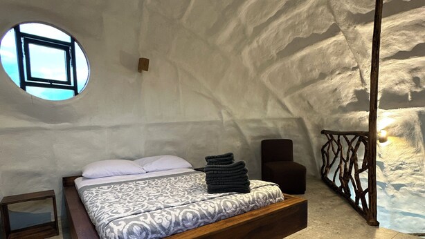 A bedroom with a wooden bed, a circular window, and a stone wall. - Animal Glamping (Pomona)