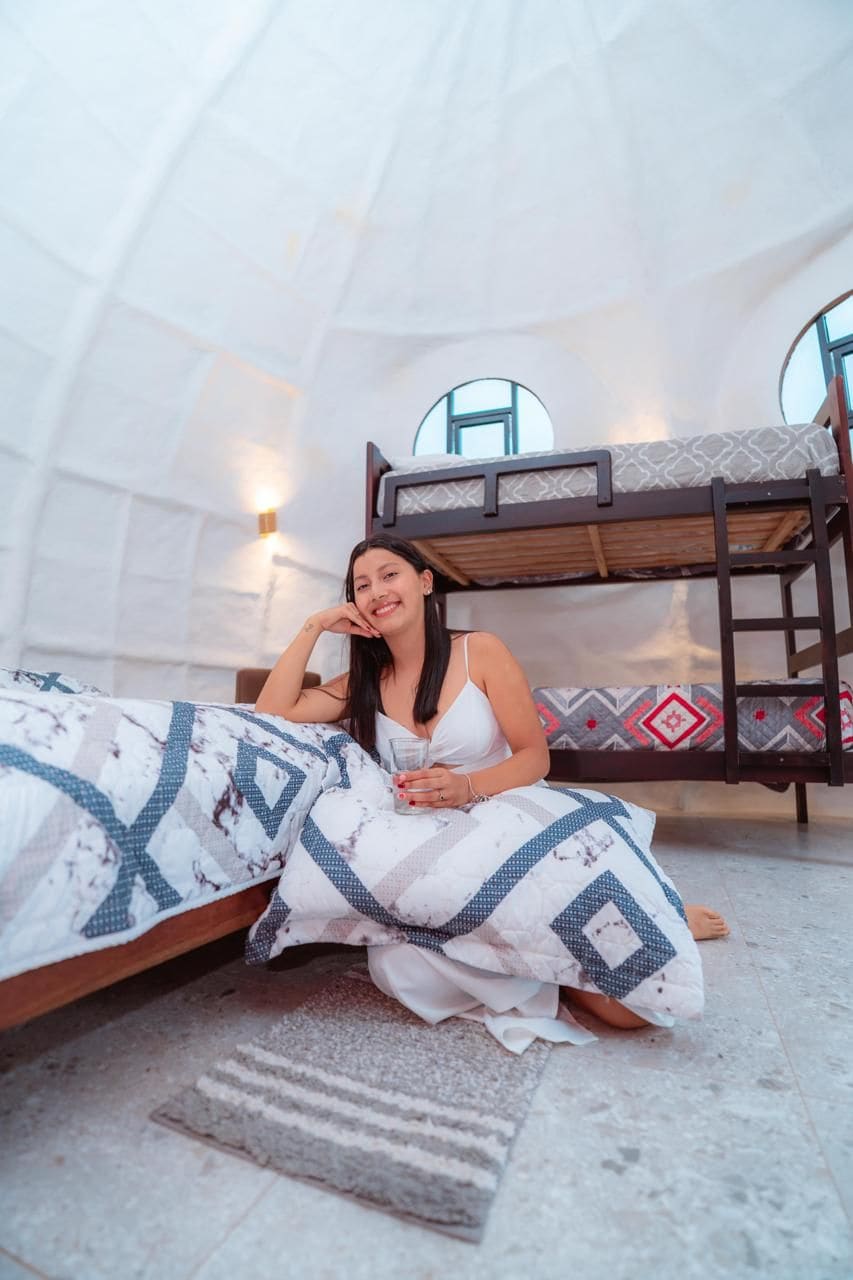 A person sitting on a bed in a room with a bunk bed and a wall-mounted light fixture.