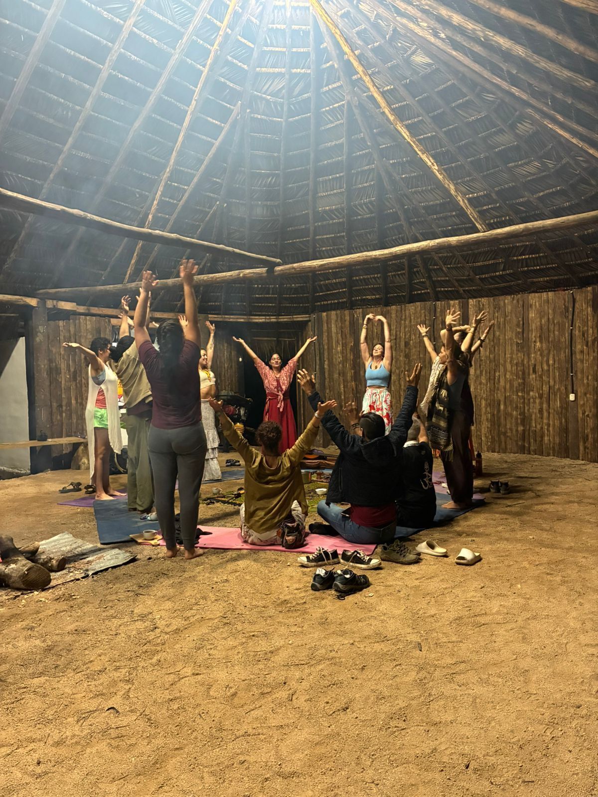 Een groep mensen doet yoga in een rustieke, open ruimte met een houten plafond.