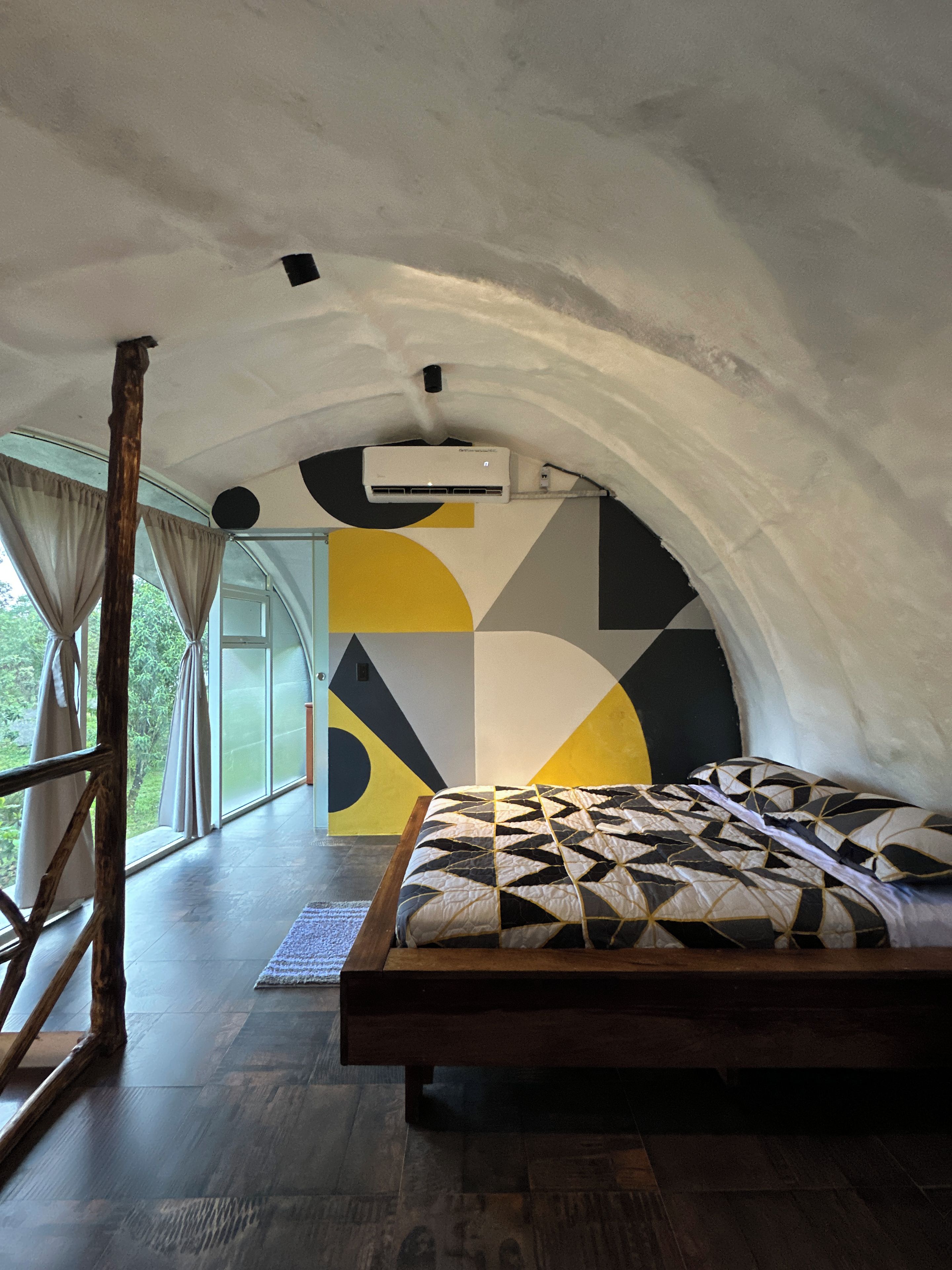 A room with a bed, an air conditioning unit, a window with curtains, and a geometric wall design.