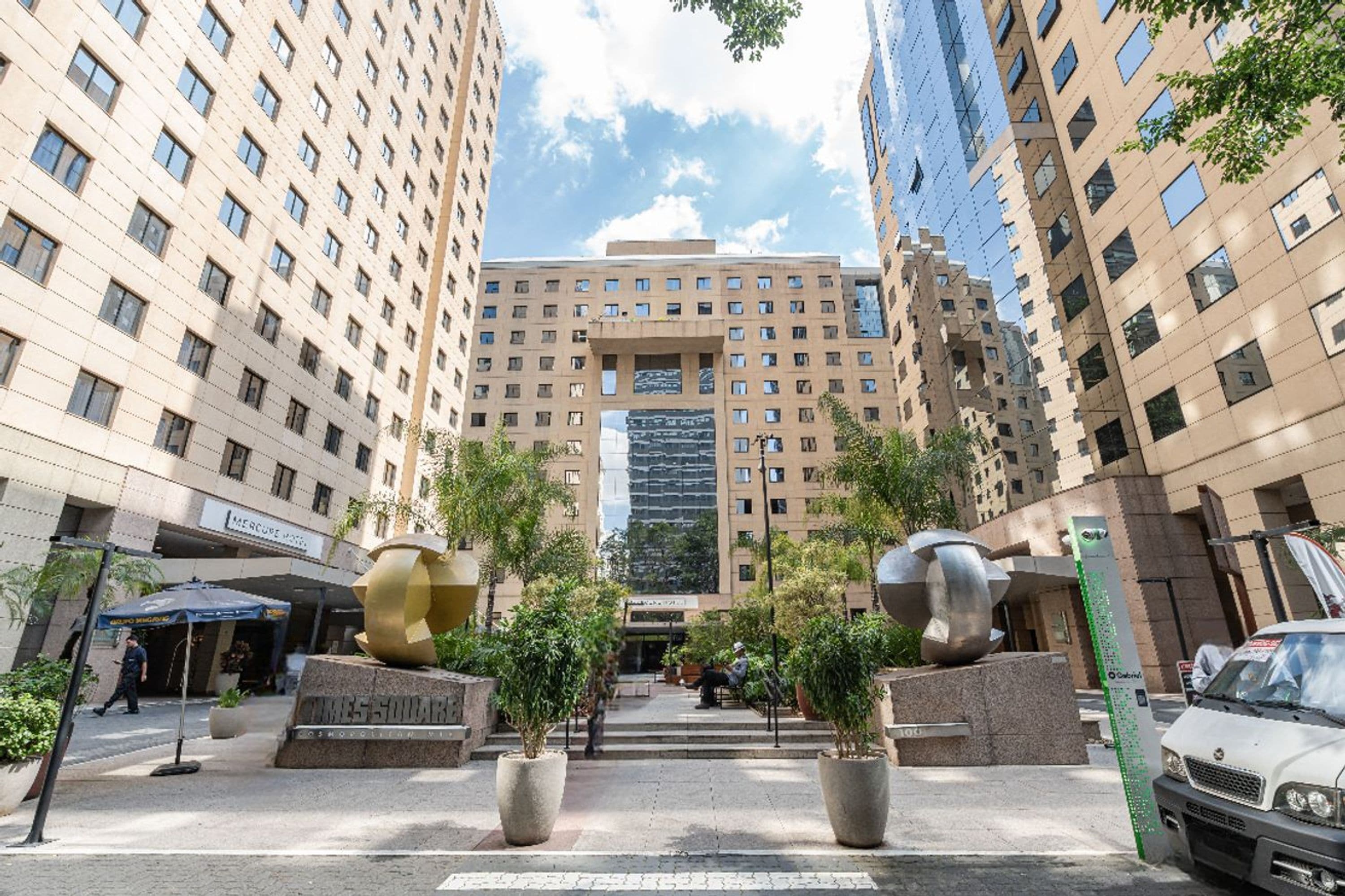 A high-rise building with a central entrance, surrounded by smaller buildings, and a clear sky.