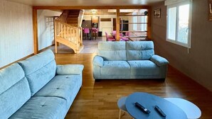 A spacious living area with a wooden staircase, two light blue sofas, and a round coffee table with remotes. - Gîte du Roc 8/10 persons (SAINT-SAUVEUR-DE-PEYRE)