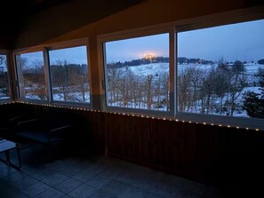 A room with large windows overlooking a snowy landscape at dusk. - Gîte du Roc (8–10 people) (SAINT-SAUVEUR-DE-PEYRE)