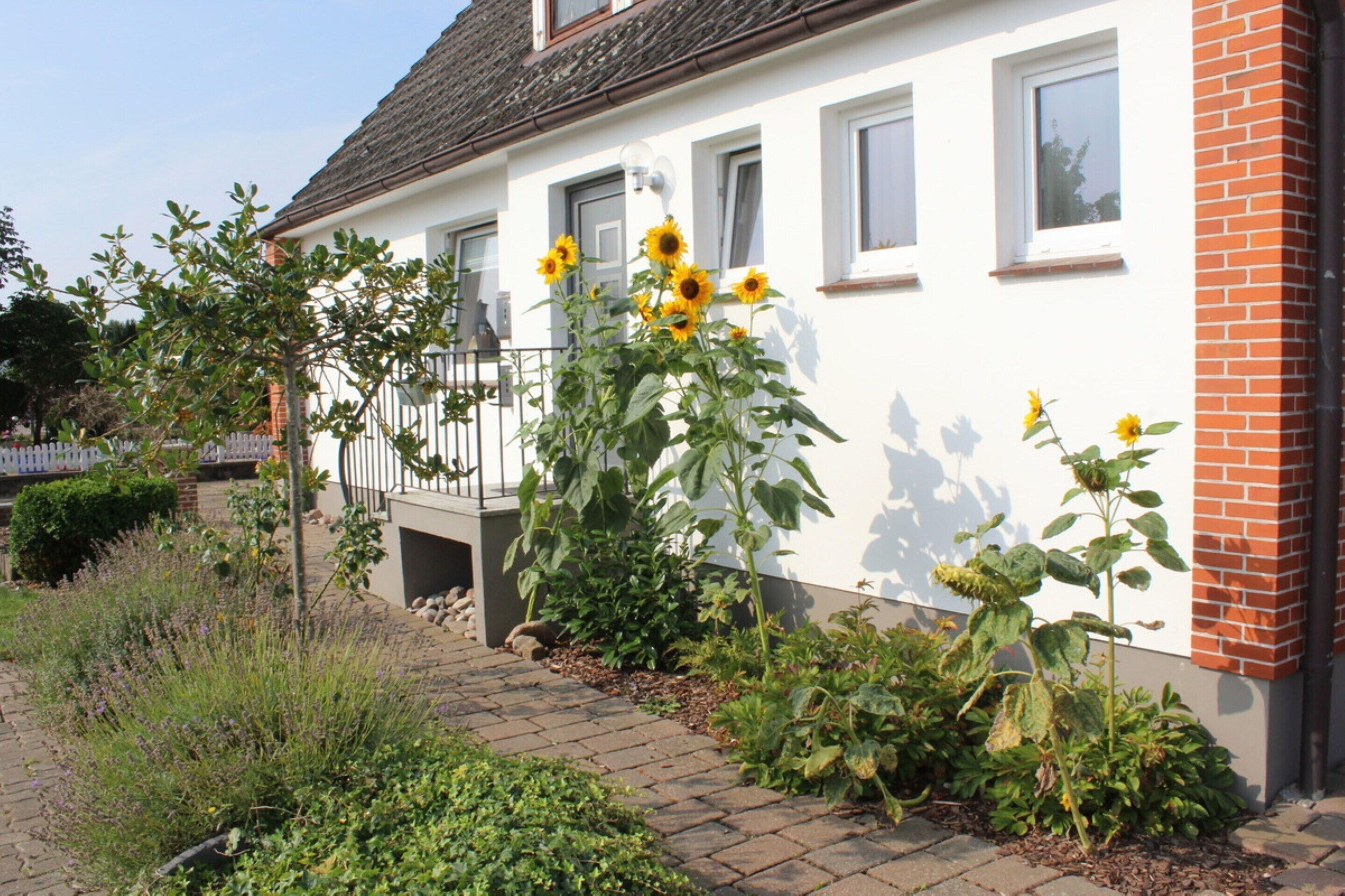 Ein weißes Haus mit Backsteinanteil, einem Balkon und Sonnenblumen im Garten.