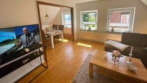 A modern living room with a television, dining area, and large windows. - Family-friendly Stay, Ostsee (Fehmarn)