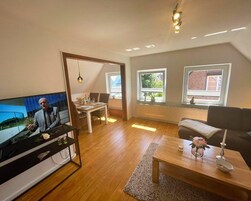 Ein modernes Wohnzimmer mit Fernseher, Essbereich und großen Fenstern.
