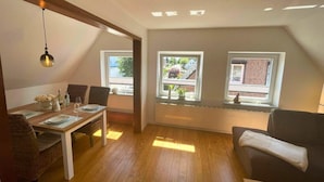 A dining area with a table set for two, a sofa, and two windows with views of a residential area. - Family-friendly Stay, Ostsee (Fehmarn)